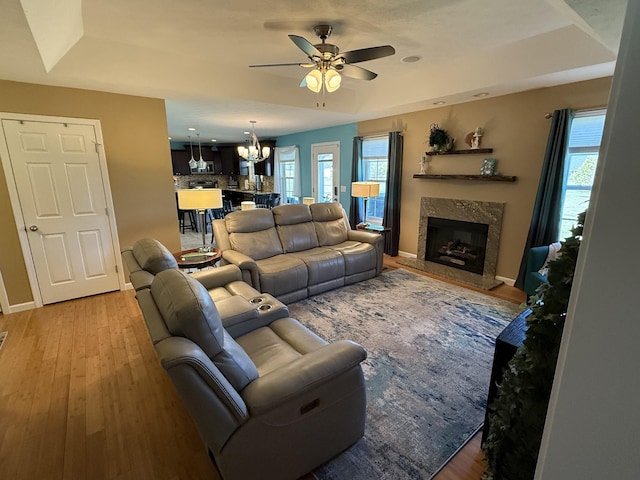 living area with light wood-type flooring, a fireplace, a wealth of natural light, and ceiling fan with notable chandelier