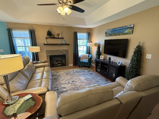 living area featuring ceiling fan, a tray ceiling, and a high end fireplace