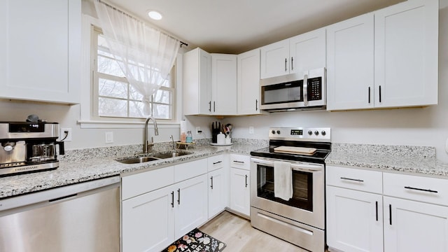 kitchen with appliances with stainless steel finishes, light wood-style floors, white cabinetry, a sink, and light stone countertops