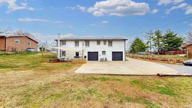 rear view of house with a garage, concrete driveway, a yard, and fence