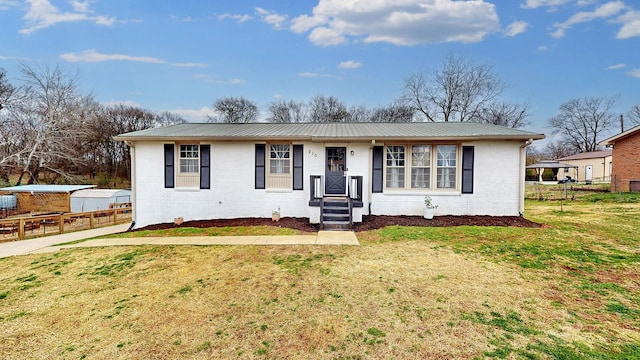 view of front of home featuring metal roof, brick siding, fence, and a front lawn