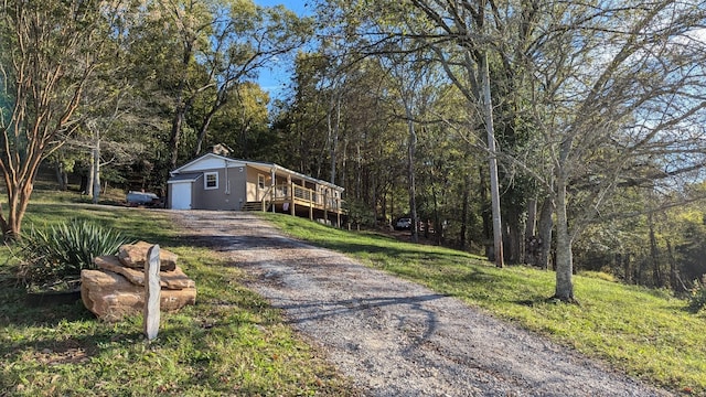 view of front of home featuring a front yard, gravel driveway, a deck, and a forest view