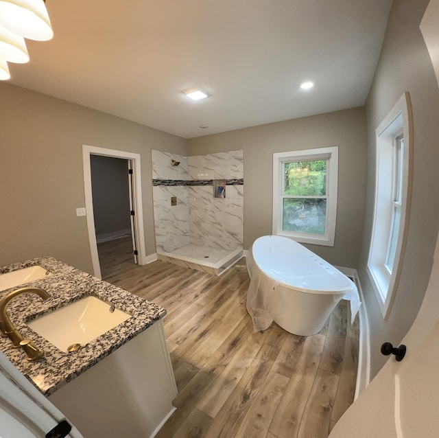 full bath featuring a sink, double vanity, a stall shower, a freestanding tub, and wood finished floors