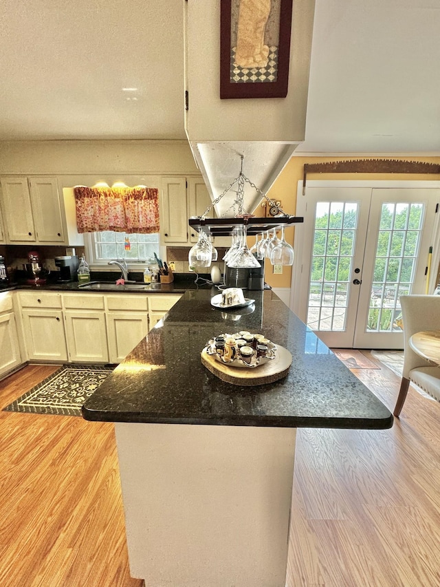 kitchen featuring dark stone counters, light wood-style flooring, french doors, a textured ceiling, and a sink