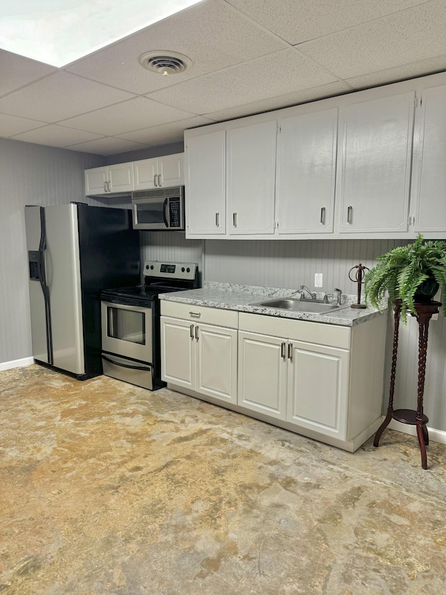 kitchen with a sink, a drop ceiling, appliances with stainless steel finishes, white cabinets, and light countertops