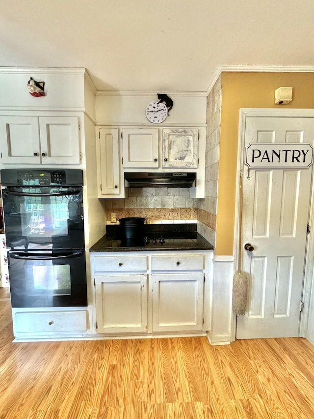 kitchen featuring black appliances, light wood-style flooring, dark countertops, and under cabinet range hood