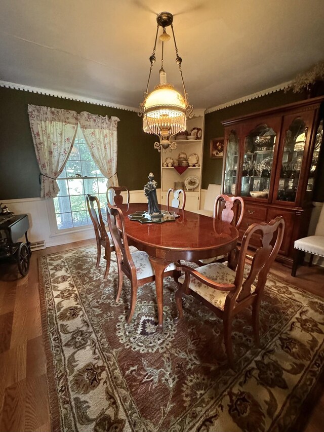 dining area with an inviting chandelier, wood finished floors, and wainscoting