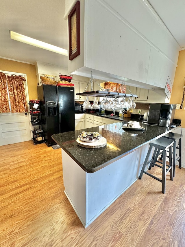 kitchen with black appliances, light wood-style flooring, dark stone countertops, and a peninsula