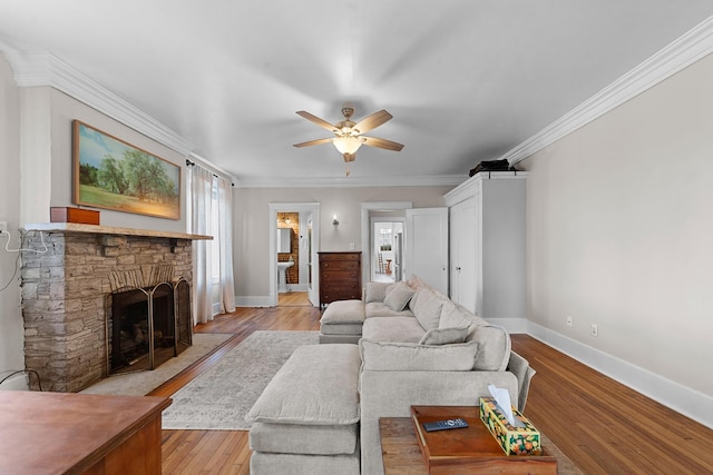 living room featuring a stone fireplace, crown molding, light wood-style flooring, and baseboards