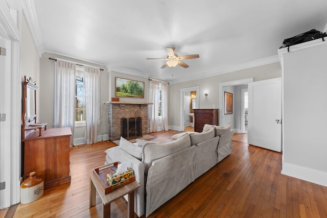 living room featuring baseboards, ornamental molding, hardwood / wood-style floors, a fireplace, and a ceiling fan