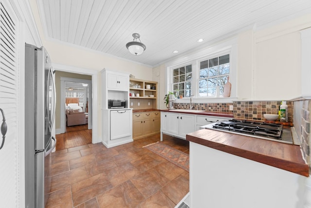 kitchen with butcher block countertops, a sink, backsplash, appliances with stainless steel finishes, and crown molding