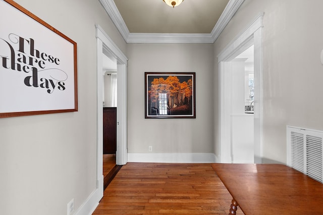 corridor featuring crown molding, wood finished floors, visible vents, and baseboards