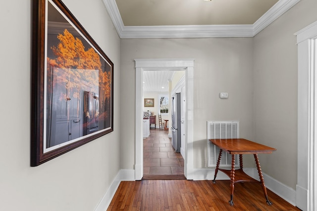 hallway with hardwood / wood-style floors, visible vents, baseboards, and ornamental molding