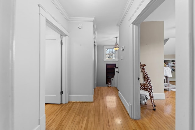 corridor with light wood finished floors, crown molding, and baseboards