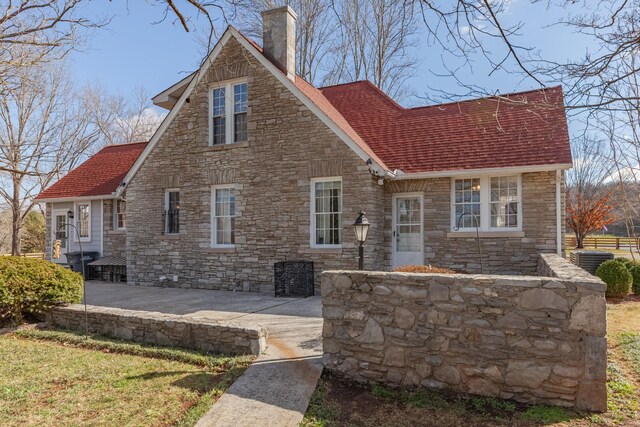 rear view of house featuring central AC unit, a chimney, and roof with shingles