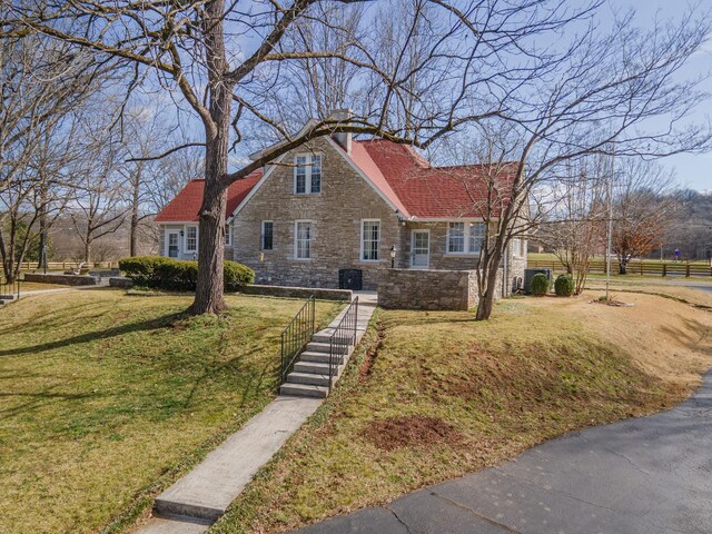 view of front of property featuring a front yard, central air condition unit, and stone siding