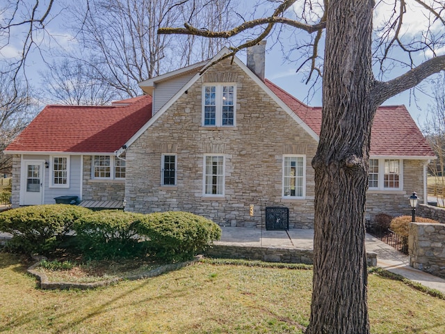 rear view of house with a patio, a lawn, roof with shingles, and a chimney