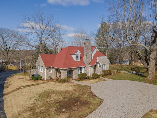 cape cod-style house with a front lawn, decorative driveway, stone siding, and a chimney