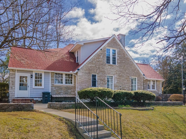 view of front facade with entry steps, a front lawn, a shingled roof, and a chimney