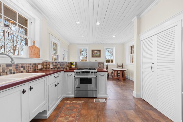 kitchen featuring visible vents, high end stainless steel range, a sink, crown molding, and decorative backsplash