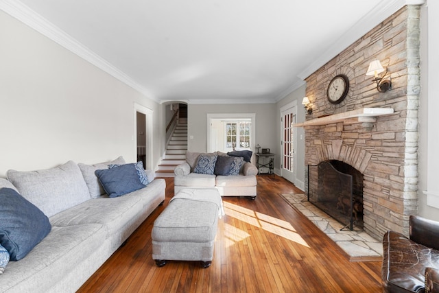 living area with a stone fireplace, crown molding, stairway, and wood-type flooring