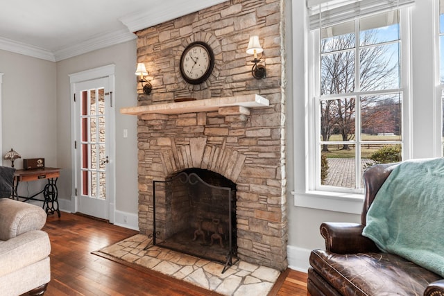 living room featuring a stone fireplace, crown molding, baseboards, and wood-type flooring