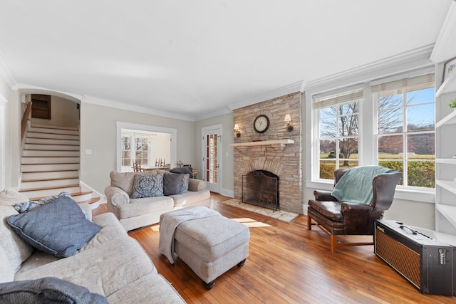 living area with light wood-type flooring, stairs, ornamental molding, a fireplace, and arched walkways