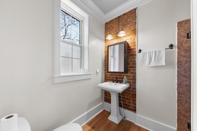 half bath featuring wood finished floors, baseboards, brick wall, crown molding, and toilet