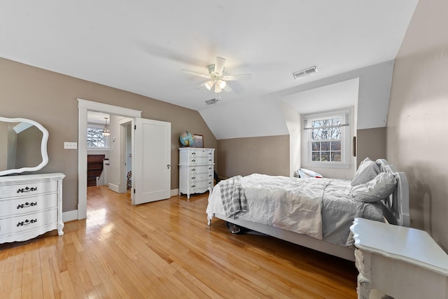 bedroom with visible vents, light wood-style floors, baseboards, ceiling fan, and vaulted ceiling