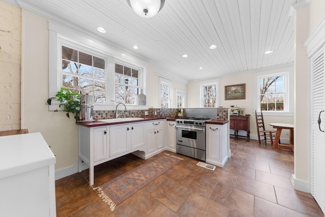 kitchen featuring a sink, high end stainless steel range oven, tasteful backsplash, white cabinetry, and a peninsula