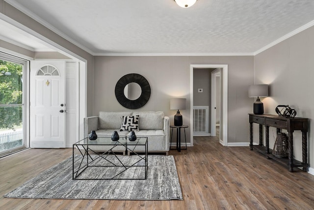 living room featuring a textured ceiling, crown molding, baseboards, and wood finished floors