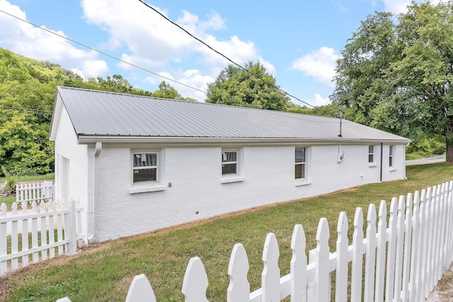 view of side of property featuring a lawn, fence private yard, brick siding, and metal roof