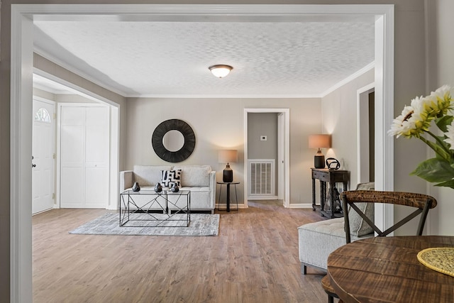 interior space featuring a textured ceiling, wood finished floors, visible vents, and ornamental molding