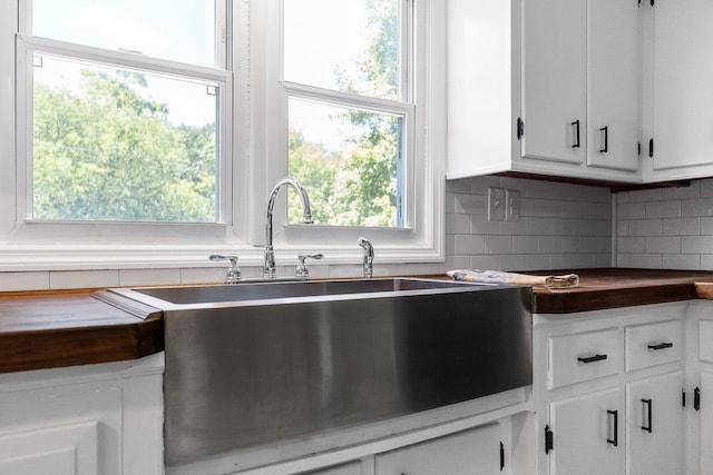 kitchen with a sink, tasteful backsplash, dark countertops, and white cabinetry