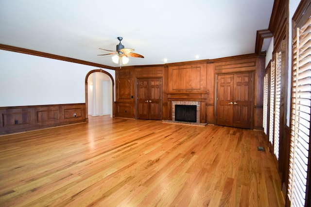 unfurnished living room with light wood-style flooring, a fireplace, arched walkways, ceiling fan, and ornamental molding