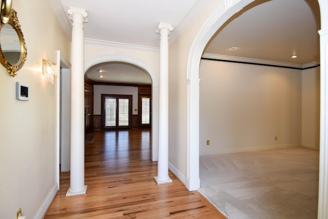 corridor with light wood-type flooring, arched walkways, crown molding, baseboards, and ornate columns