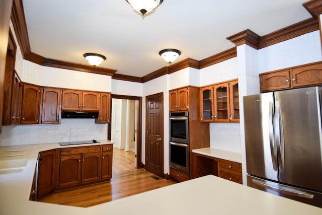 kitchen with under cabinet range hood, light countertops, ornamental molding, wood finished floors, and stainless steel appliances