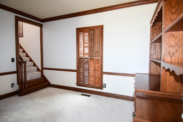 carpeted spare room with visible vents, baseboards, crown molding, and stairway