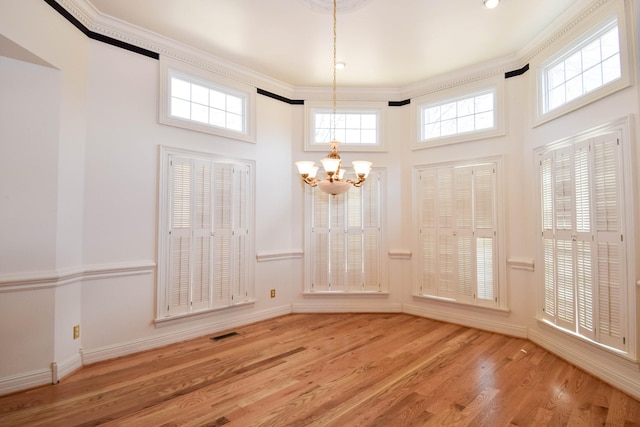 unfurnished dining area with visible vents, crown molding, baseboards, wood finished floors, and a notable chandelier