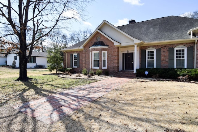 view of front of home with brick siding, a chimney, a front yard, and roof with shingles