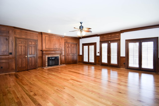 unfurnished living room featuring wooden walls, a ceiling fan, crown molding, a brick fireplace, and light wood-type flooring