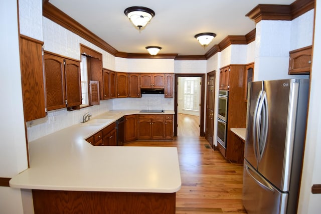 kitchen with black appliances, light wood-style flooring, a peninsula, crown molding, and light countertops