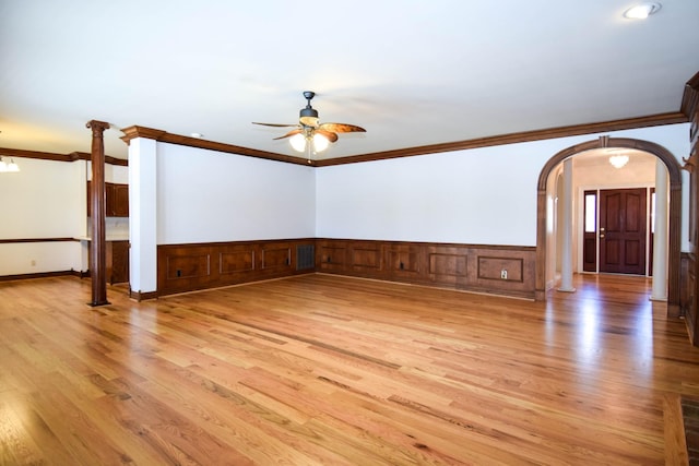 spare room with light wood-style flooring, ceiling fan with notable chandelier, arched walkways, and wainscoting