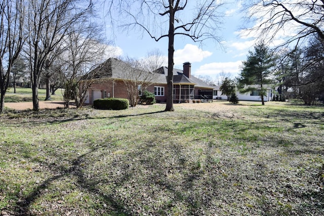 exterior space featuring brick siding, an attached garage, a chimney, and a yard