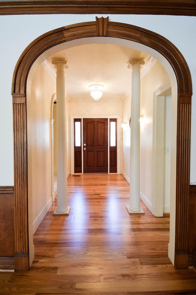 entrance foyer featuring light wood-style floors, arched walkways, and ornate columns