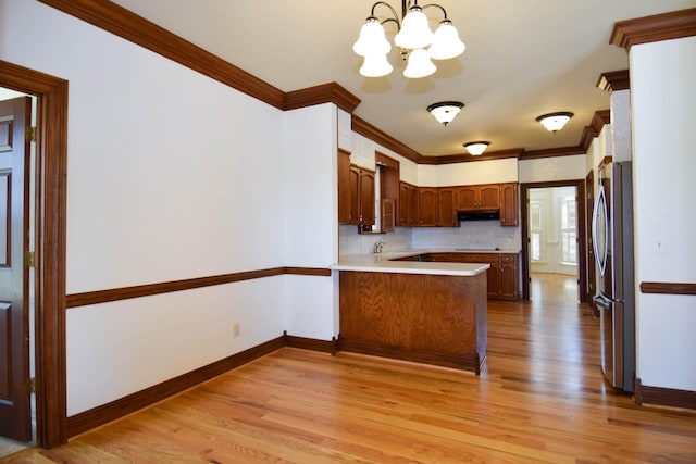 kitchen with crown molding, under cabinet range hood, light wood-type flooring, a peninsula, and freestanding refrigerator