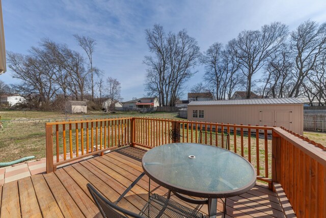 deck with outdoor dining space, an outbuilding, fence, a shed, and a lawn