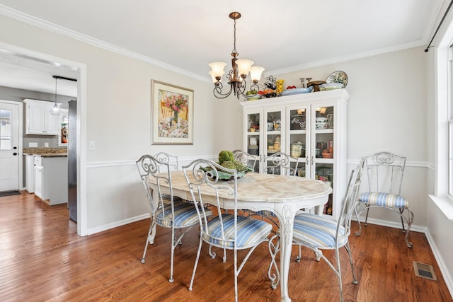 dining space featuring visible vents, crown molding, an inviting chandelier, and wood finished floors