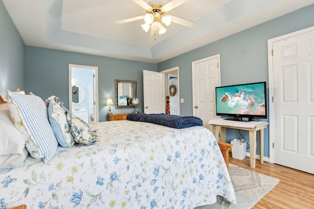 bedroom featuring wood finished floors, baseboards, ceiling fan, ensuite bathroom, and a raised ceiling