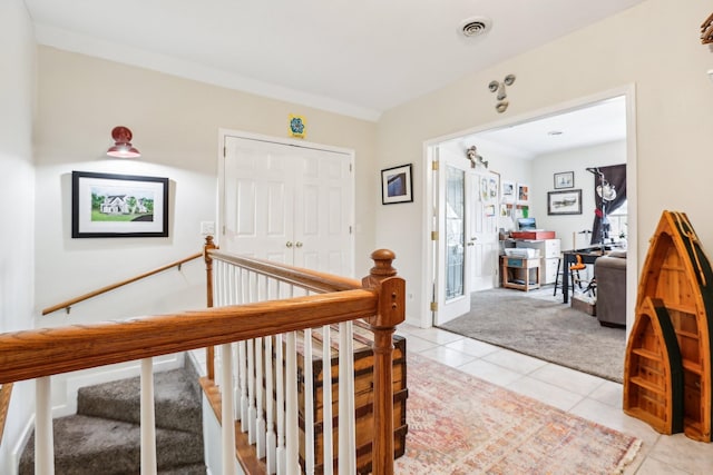 hallway with light tile patterned floors, light colored carpet, visible vents, and an upstairs landing